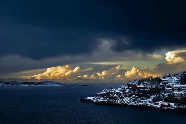 Häuser an der schneebedeckten Küste vor dem Hintergrund riesiger Wolken